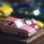 vue de face collection de voitures jouets colorées en métal assorties assise sur le bord d'une table avec une table rose à l'avant mise au point sélective lumière naturelle