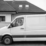 Vue latérale d'une camionnette de livraison blanche garée à l'extérieur d'une maison résidentielle avec un conducteur lisant un document.