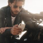 Biker tenant son téléphone, en utilisant l'application pour trouver le meilleur itinéraire, assis sur Moto Bike