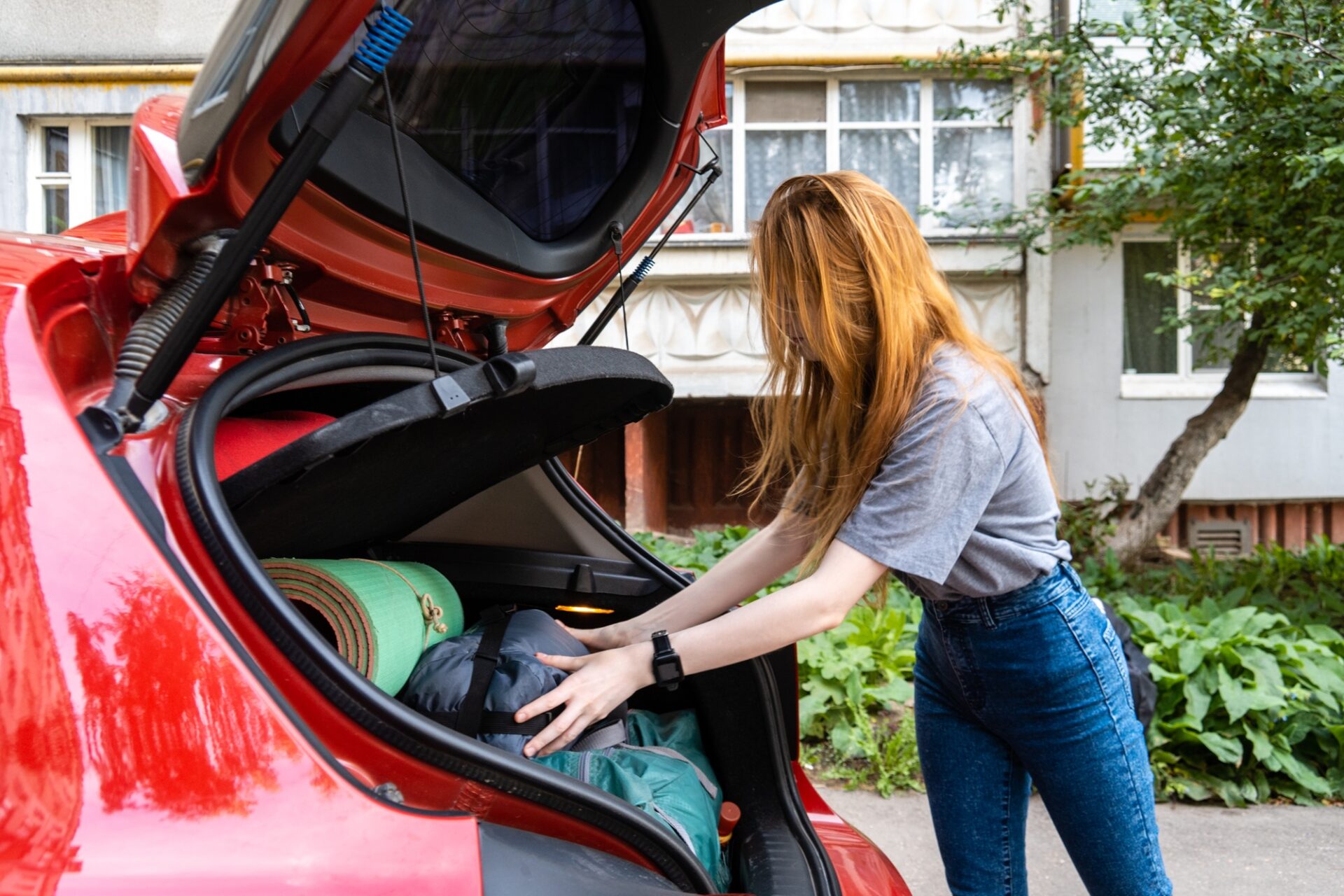 Vue latérale de la jeune femme mettant des accessoires de camping dans la voiture.