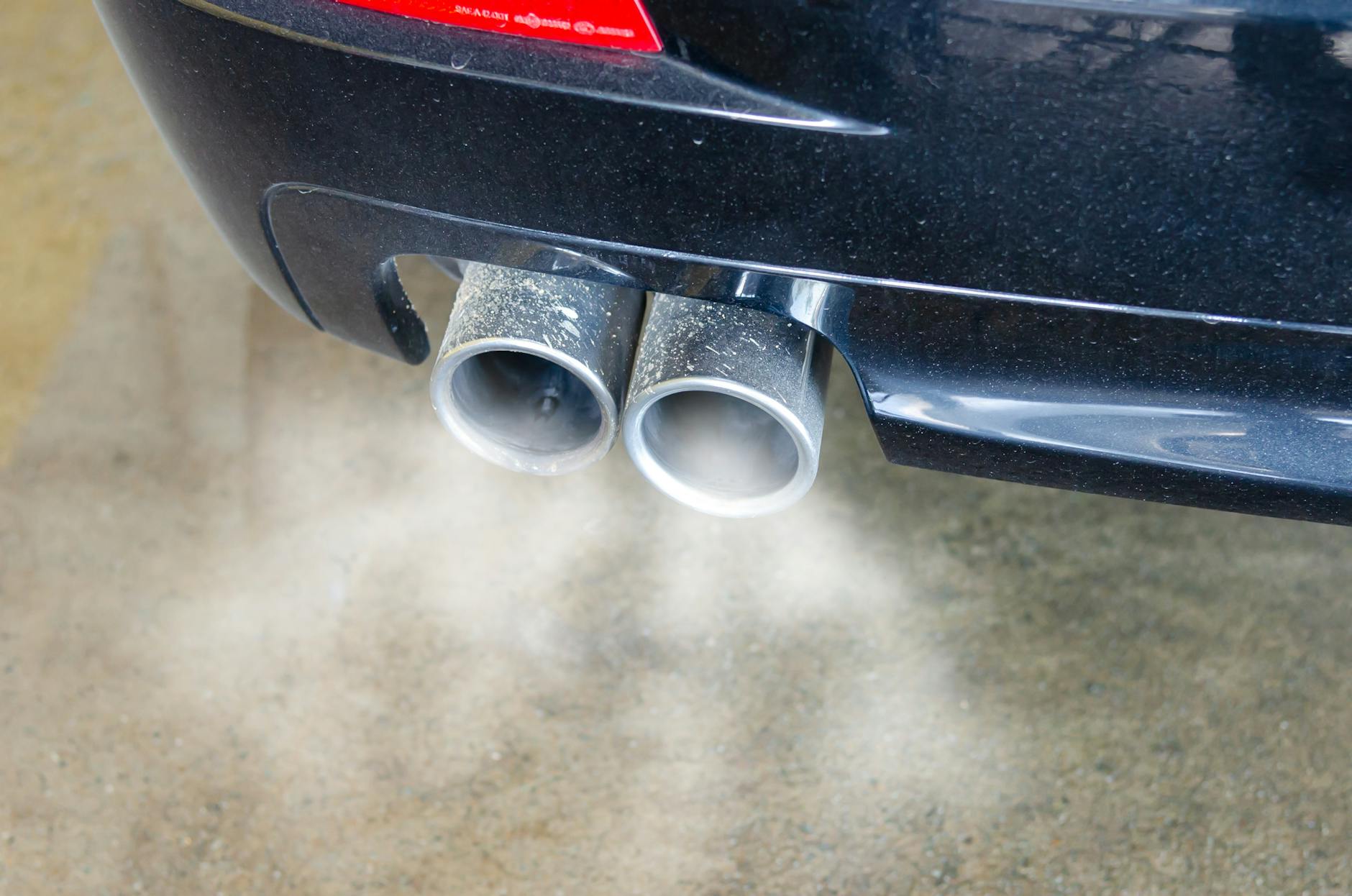 Gros plan des tuyaux d'échappement d'une voiture émettant de la fumée visible, mettant en évidence la pollution atmosphérique.