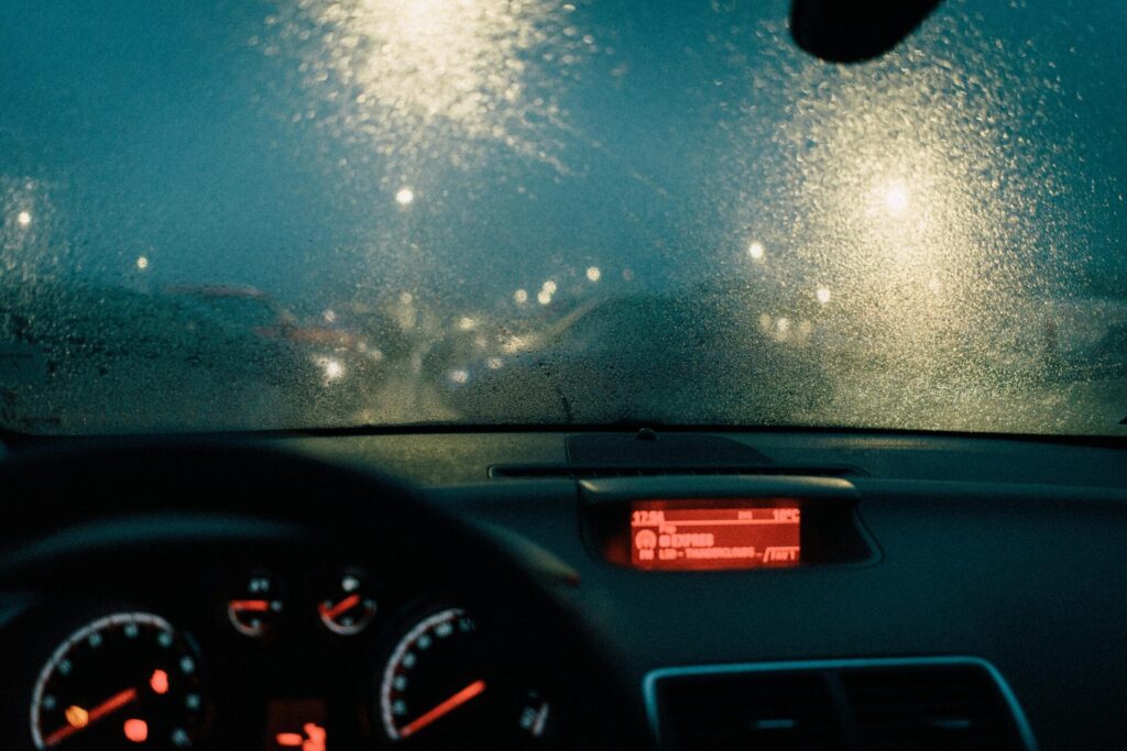 Vue depuis l'intérieur de la voiture avec des gouttes de pluie sur le pare-brise et des lumières floues la nuit.